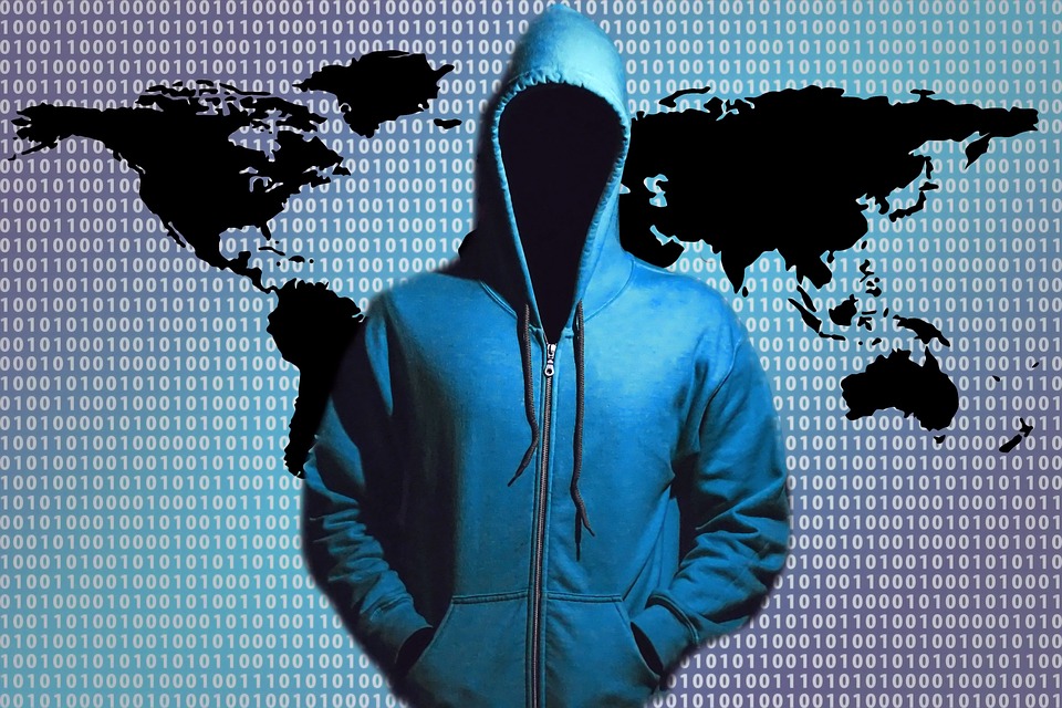 Figure in a hoodie sweatshirt standng in front of binary code (1s and 0s) over a world map