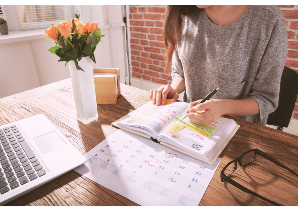 An individual writing in a notebook by a calendar
