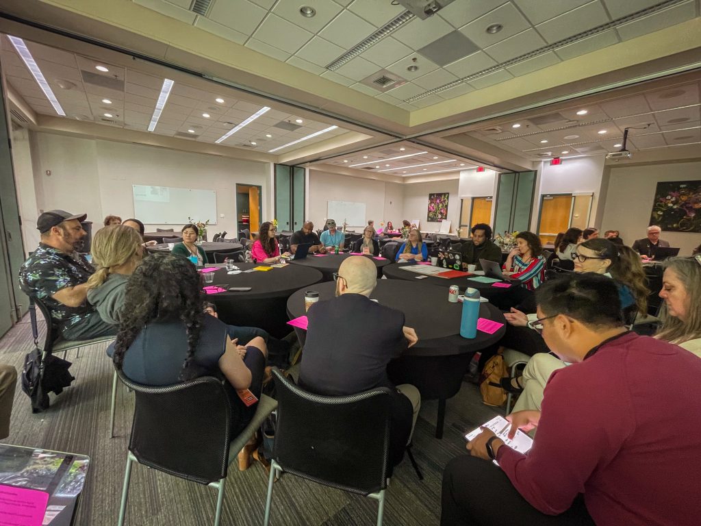 Photo of a large room full of round tables with several people sitting at each table