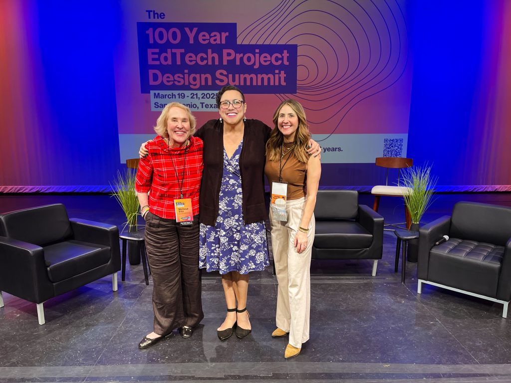 Three professionally dressed individuals stand in front of a sign that reads "100 Year EdTech Project Design Summit"