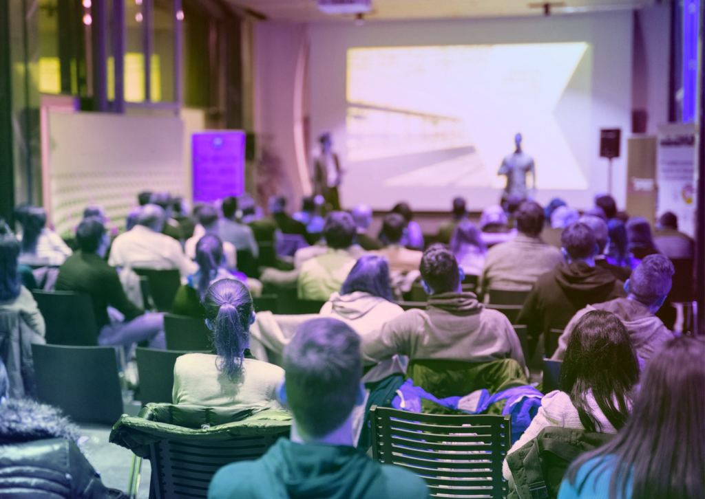 A large room full of individuals listening to a presentation 